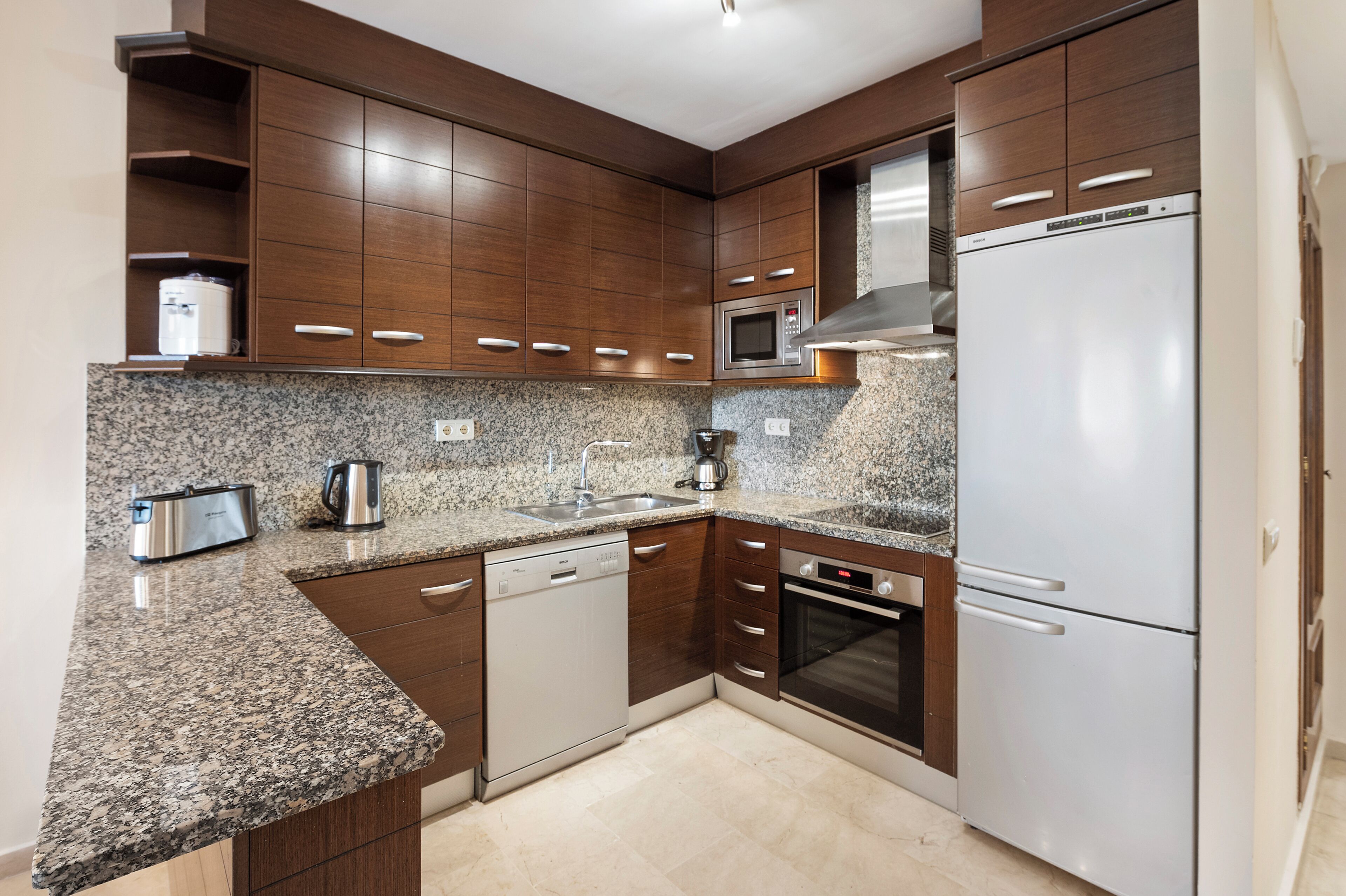 Una cocina moderna con encimeras de granito, electrodomésticos de acero inoxidable y armarios de madera.