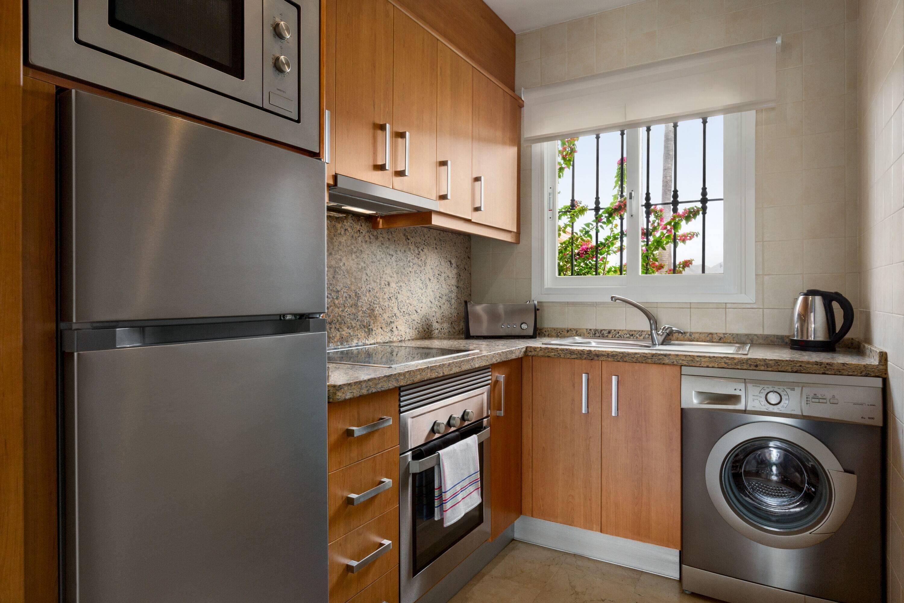 A kitchen with stainless steel appliances, wooden cabinets, a window with a view, and a built-in washing machine.