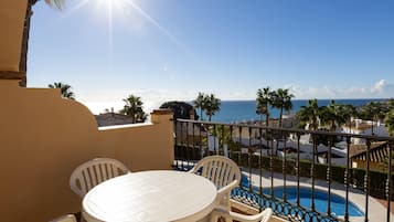 Un balcón con una mesa y sillas blancas, con vista a una piscina y al mar.