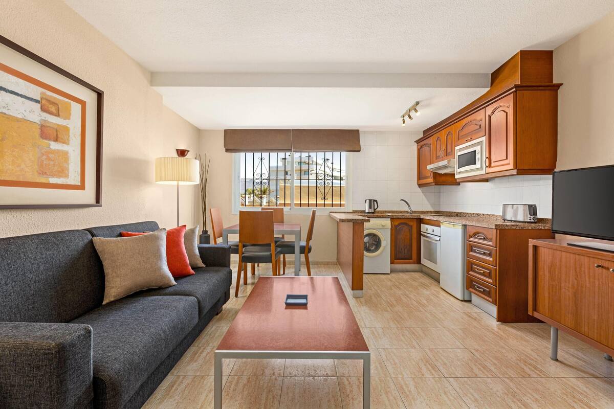 Espai vital compacte amb sofà, taula de dinar, zona de cuina i finestra amb vistes.