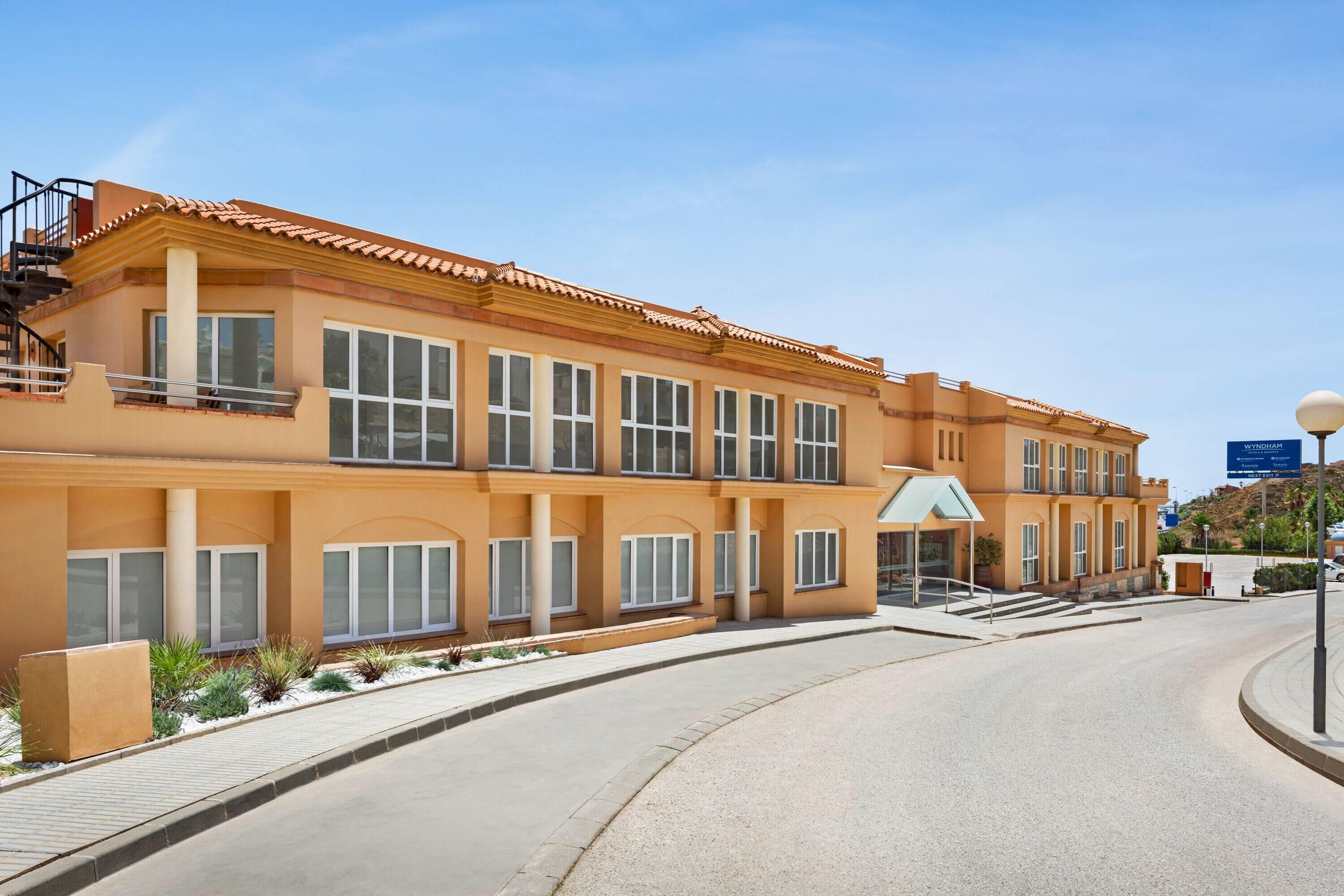 A multi-story hotel with a curved driveway, large windows, and a clear sky.