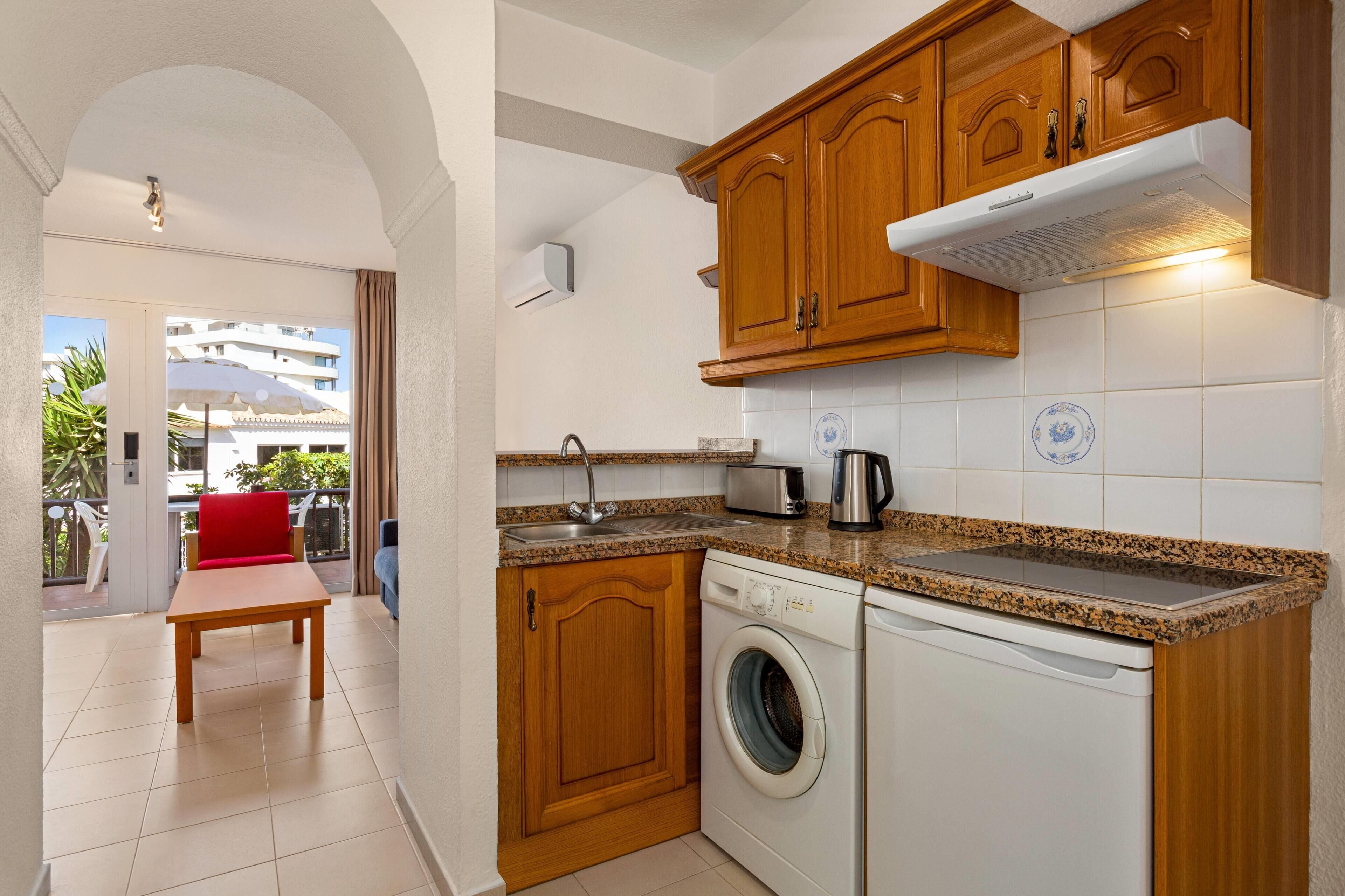 Une cuisine compacte avec des meubles en bois, un lave-linge et un coin repas agrémenté d’une chaise rouge.