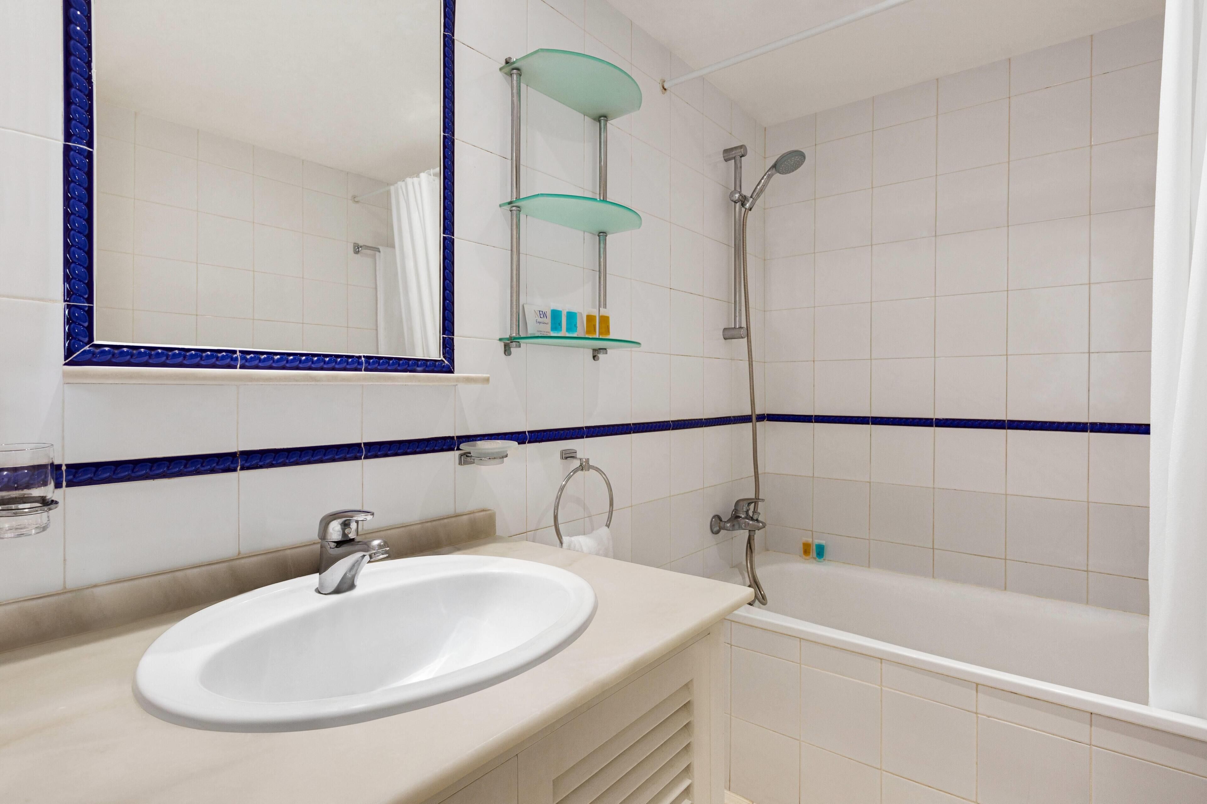Un baño con lavamanos, espejo, repisas de vidrio y ducha.
