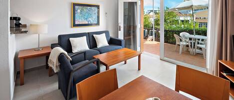 A modern living room with a sofa, coffee table, and dining table. There is a sliding glass door leading to an outdoor patio with a table and chairs.