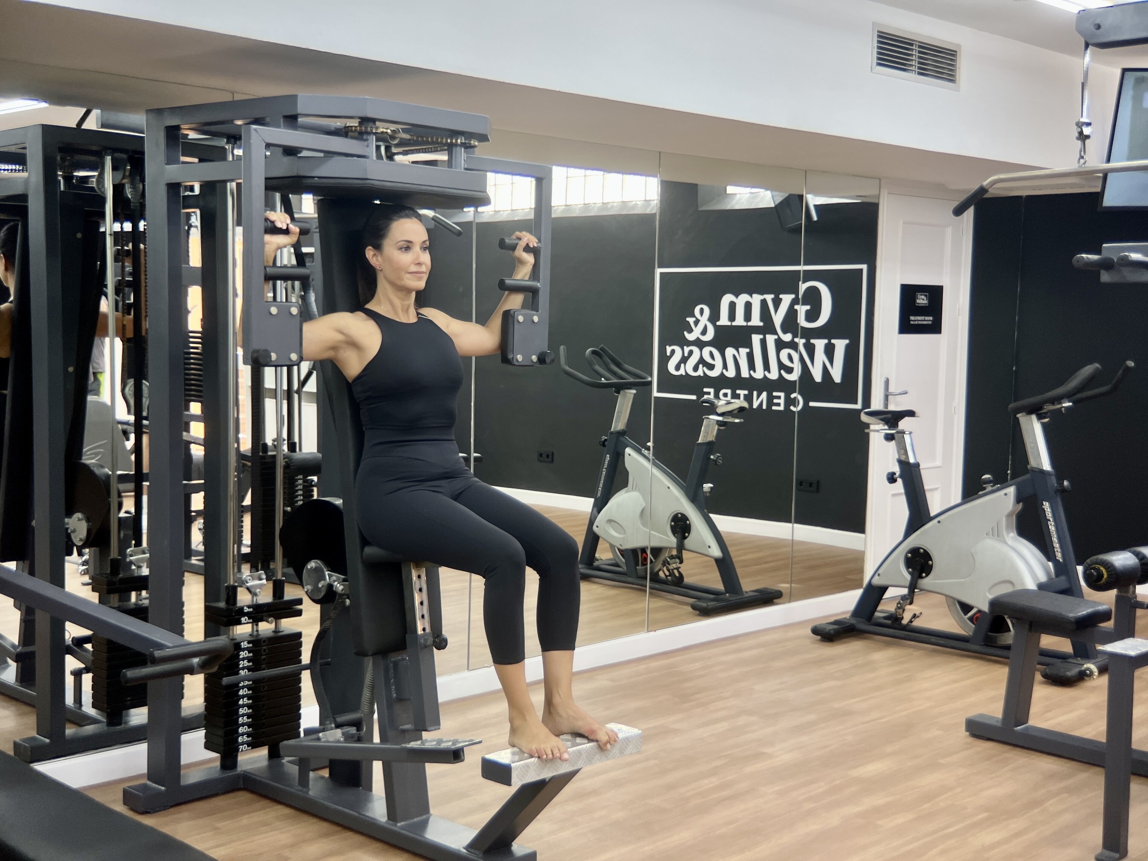 A gym with exercise equipment, a mirror, and a sign that reads "Gym & Wellness Centre".