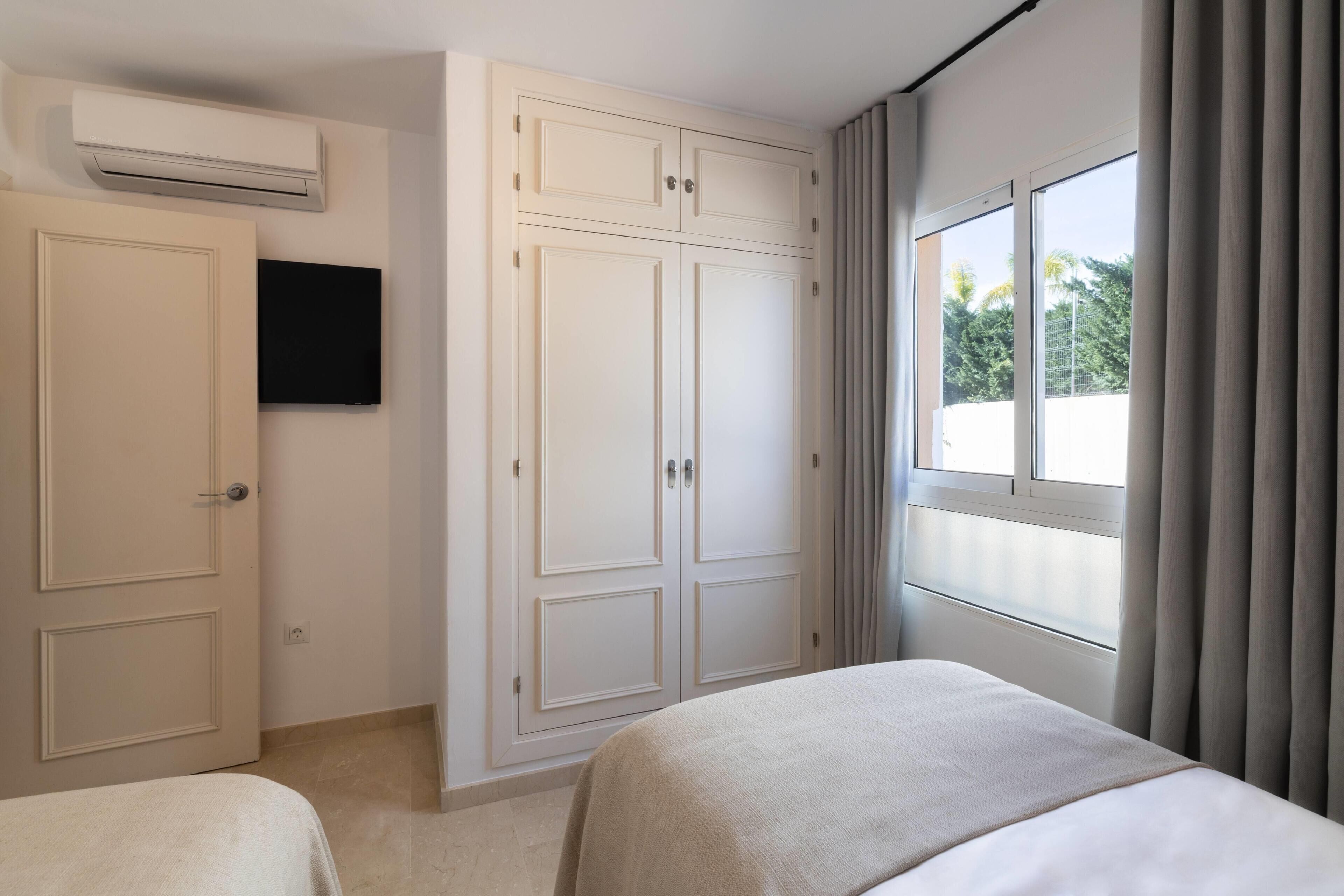 A bedroom with a bed, a wardrobe, a TV, and a window with curtains.