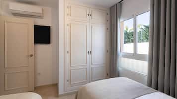 Un dormitorio con cama, armario, televisor y ventana con cortinas.