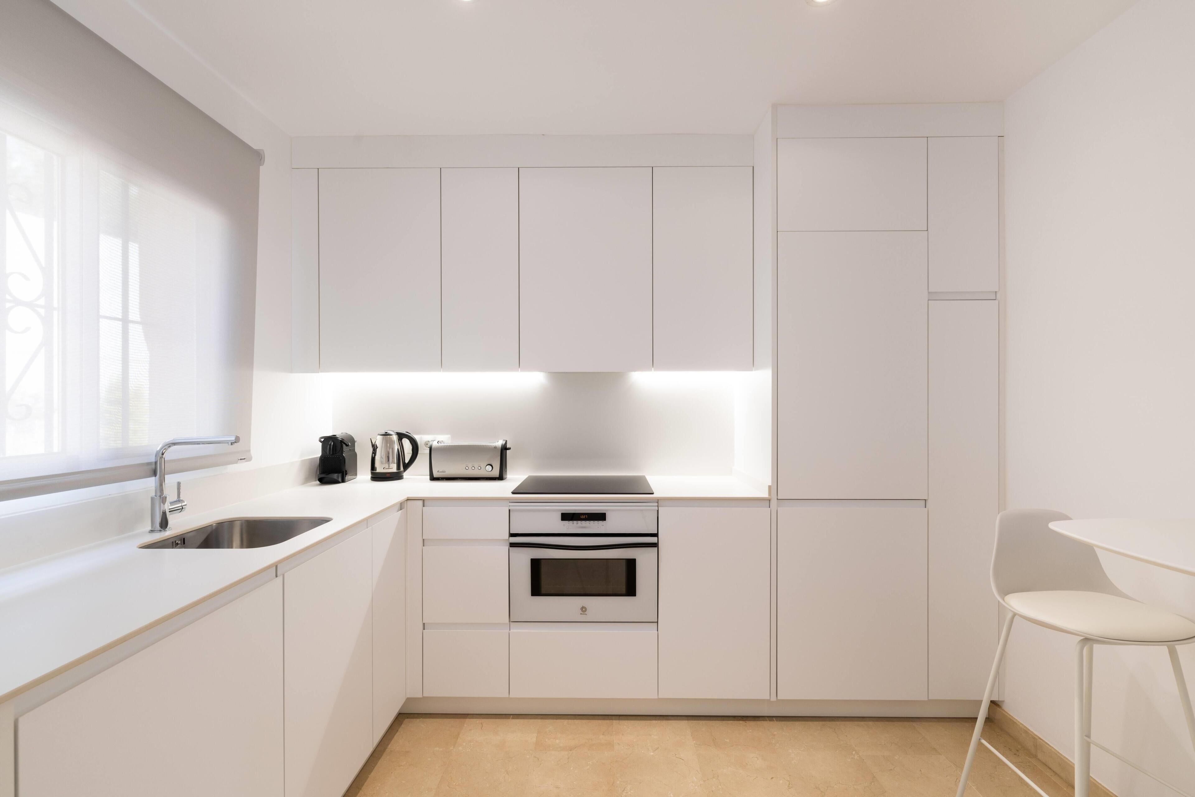 A modern kitchen with white cabinetry, a built-in oven, a coffee maker, and a toaster.