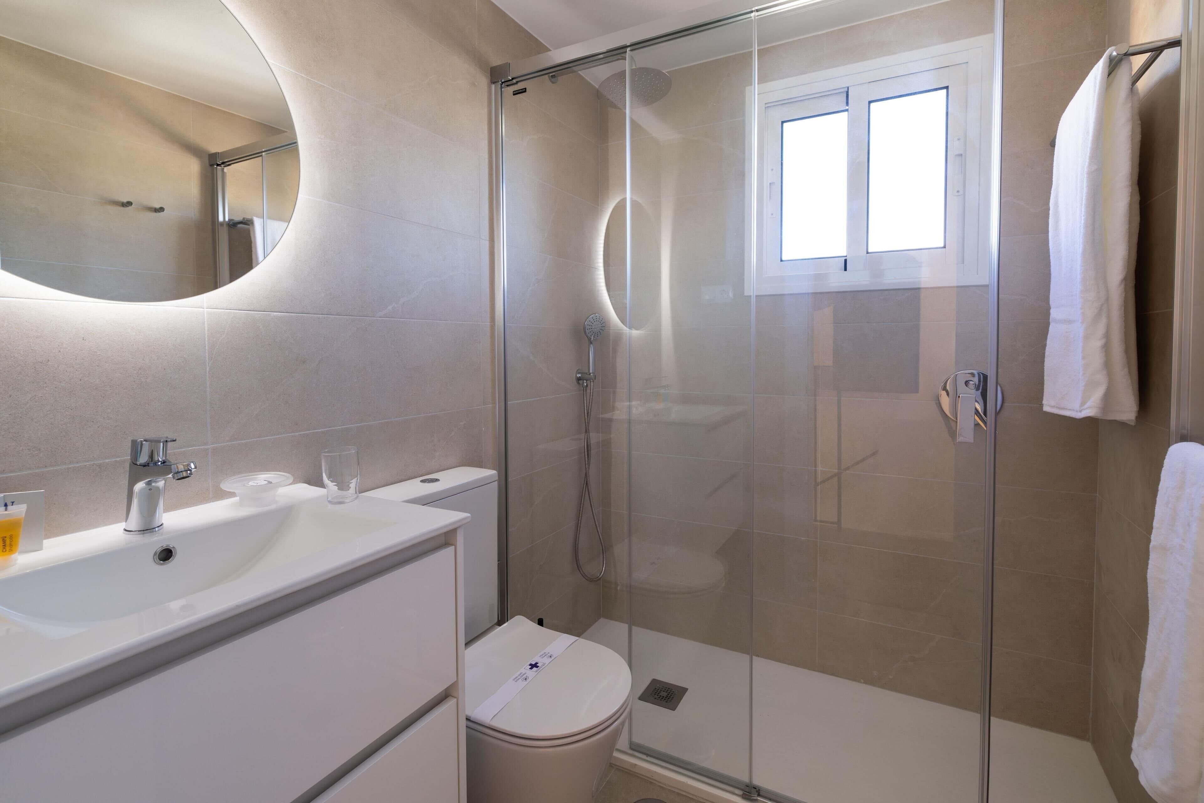 Een moderne badkamer met een douchecabine van glas, een witte wastafel en een grote spiegel.