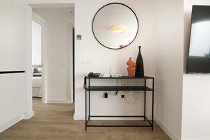 A modern room with a black metal console table, a round mirror, a flat-screen TV, and a door leading to another room.