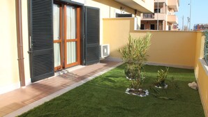 A residential building with a tiled patio, a small lawn with plants, and a sliding glass door. - La Maison Jolie (Fiumicino)