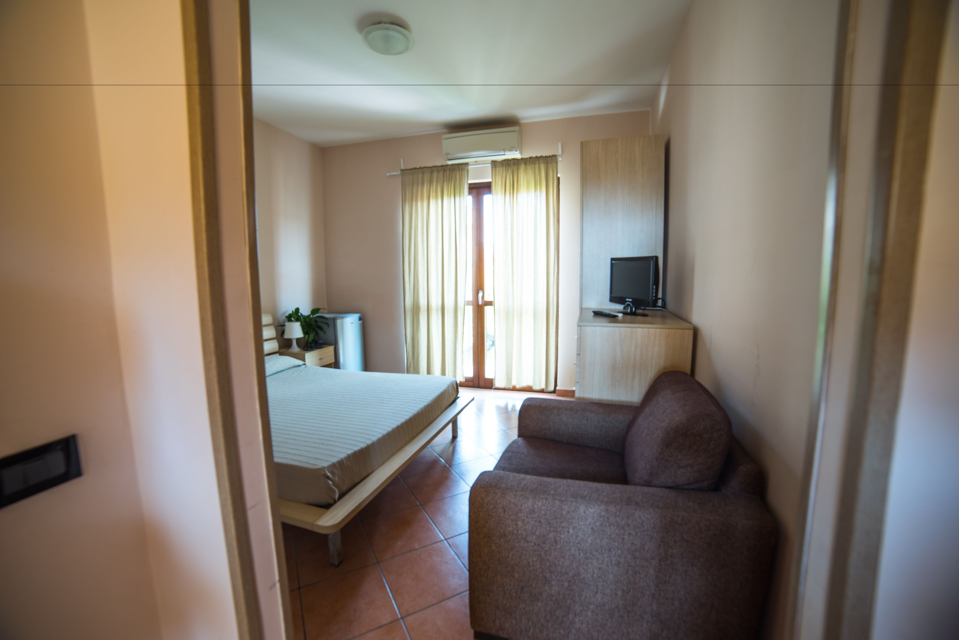 A hotel room with a bed, a sofa, a TV, and a window with curtains.