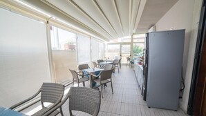 A covered outdoor dining area with wicker chairs and tables, a refrigerator, and a view of the outside. - La Maison Jolie (Fiumicino)