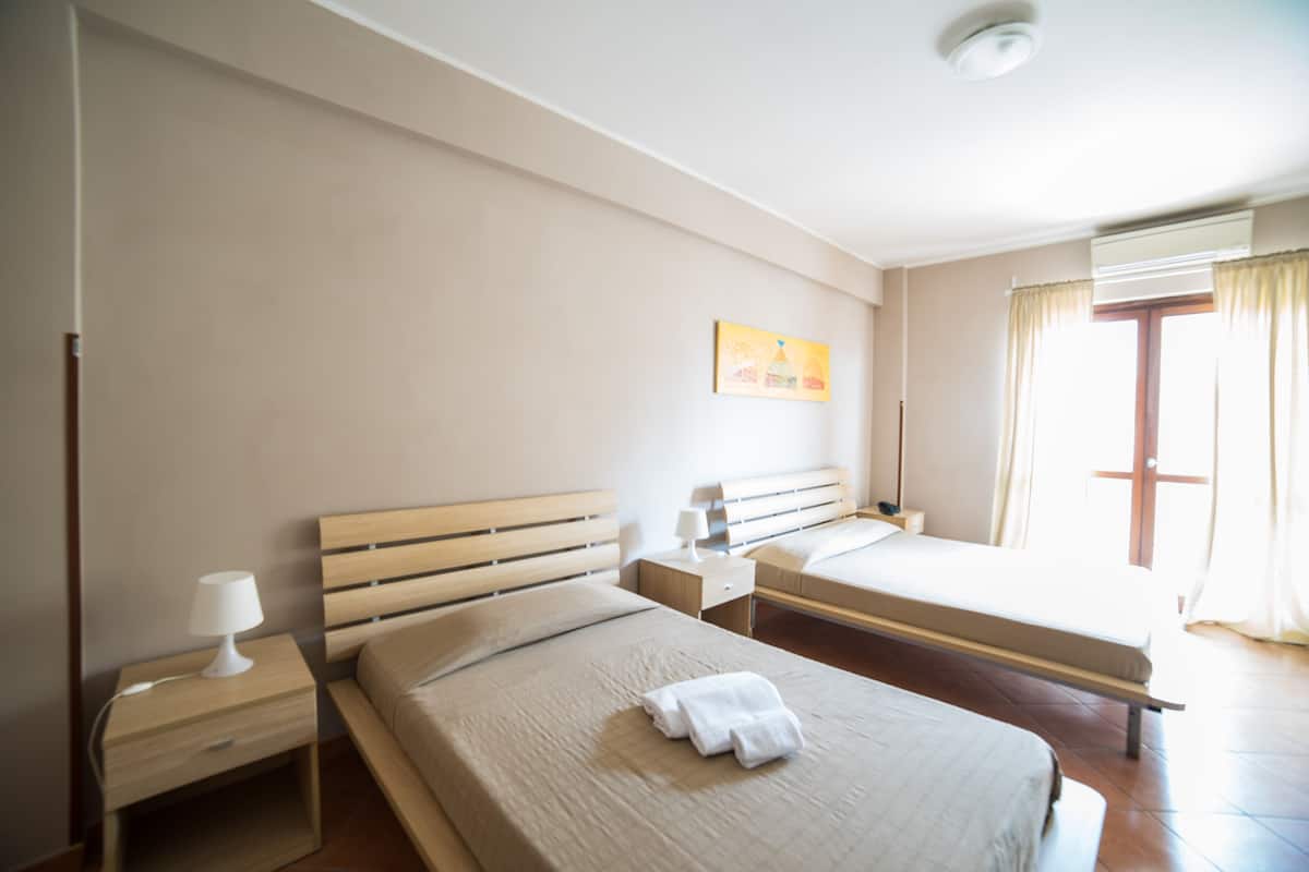 Ein Hotelzimmer mit einem großen Bett, einem kleineren Bett, einem Nachttisch mit Lampe, einem Beistelltisch und einem Gemälde an der Wand.
