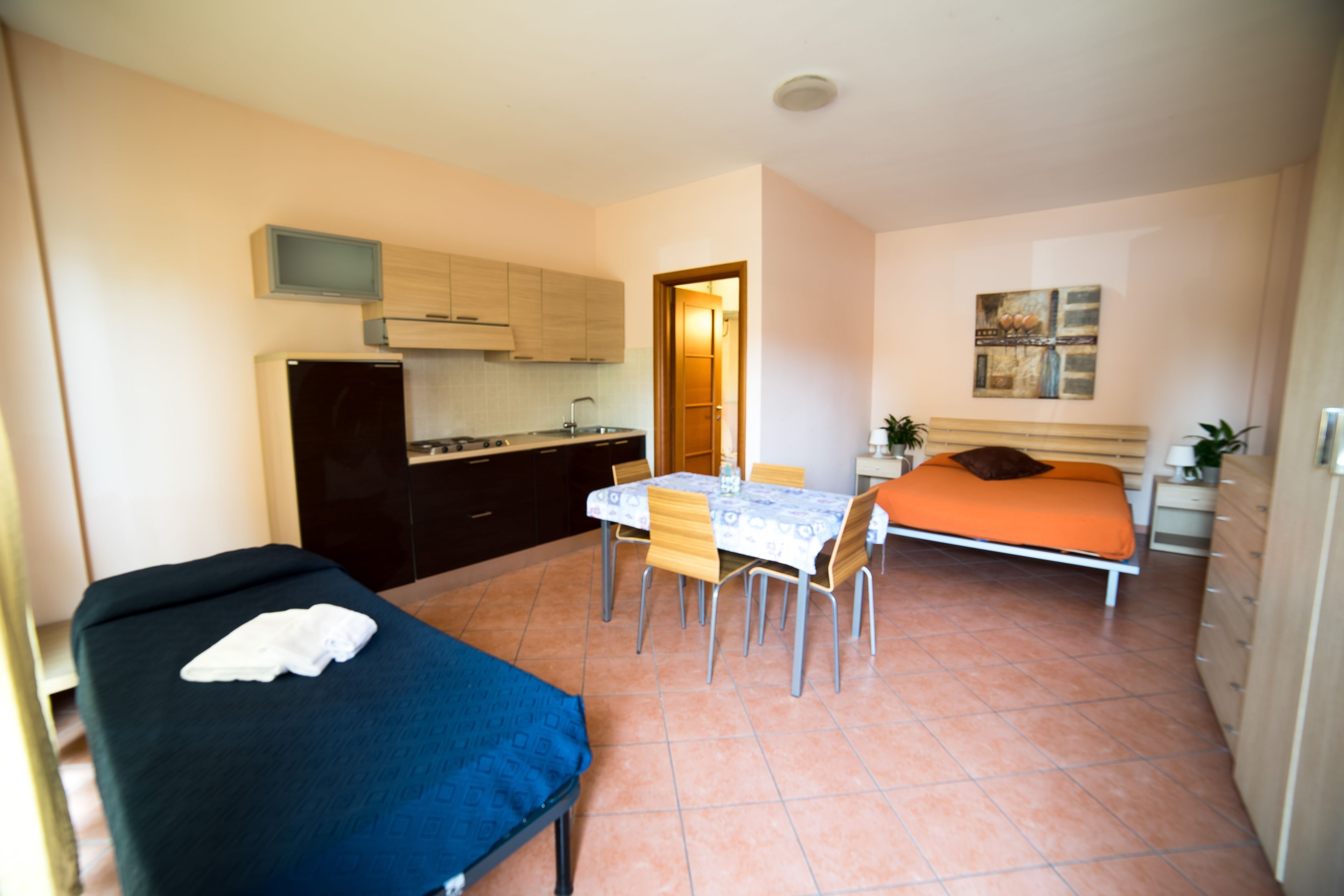 Une pièce de taille modeste comprenant un lit, une petite table avec des chaises, un coin cuisine et une salle de bain.