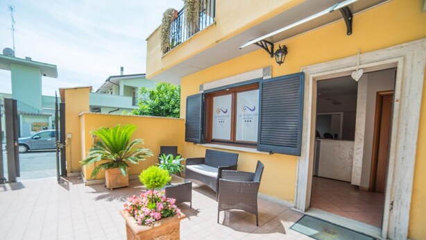 A yellow building with a balcony, outdoor seating, and potted plants. - La Maison Jolie (Fiumicino)