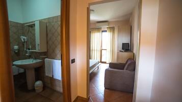 A hotel room with a bathroom, a bed, a TV, and a seating area.
