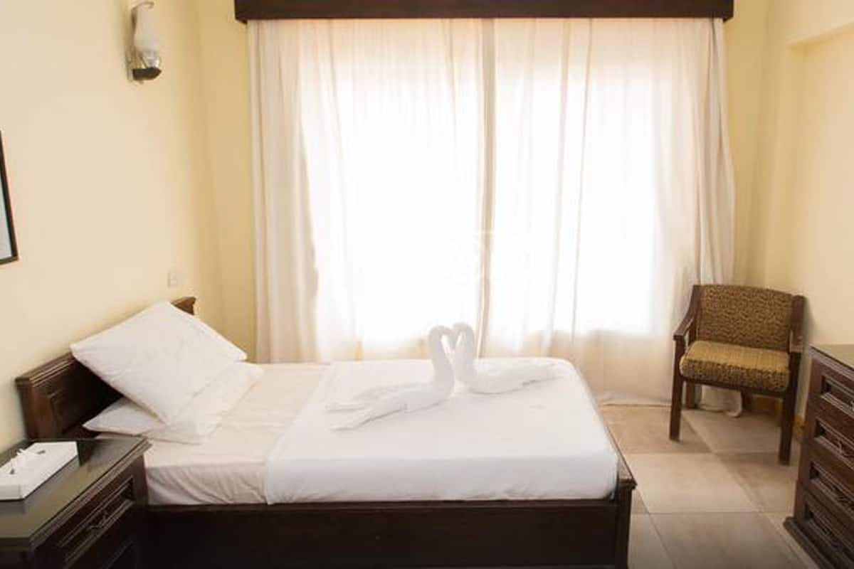 A hotel room with a neatly made bed, a chair, a dresser, and a framed picture on the wall.