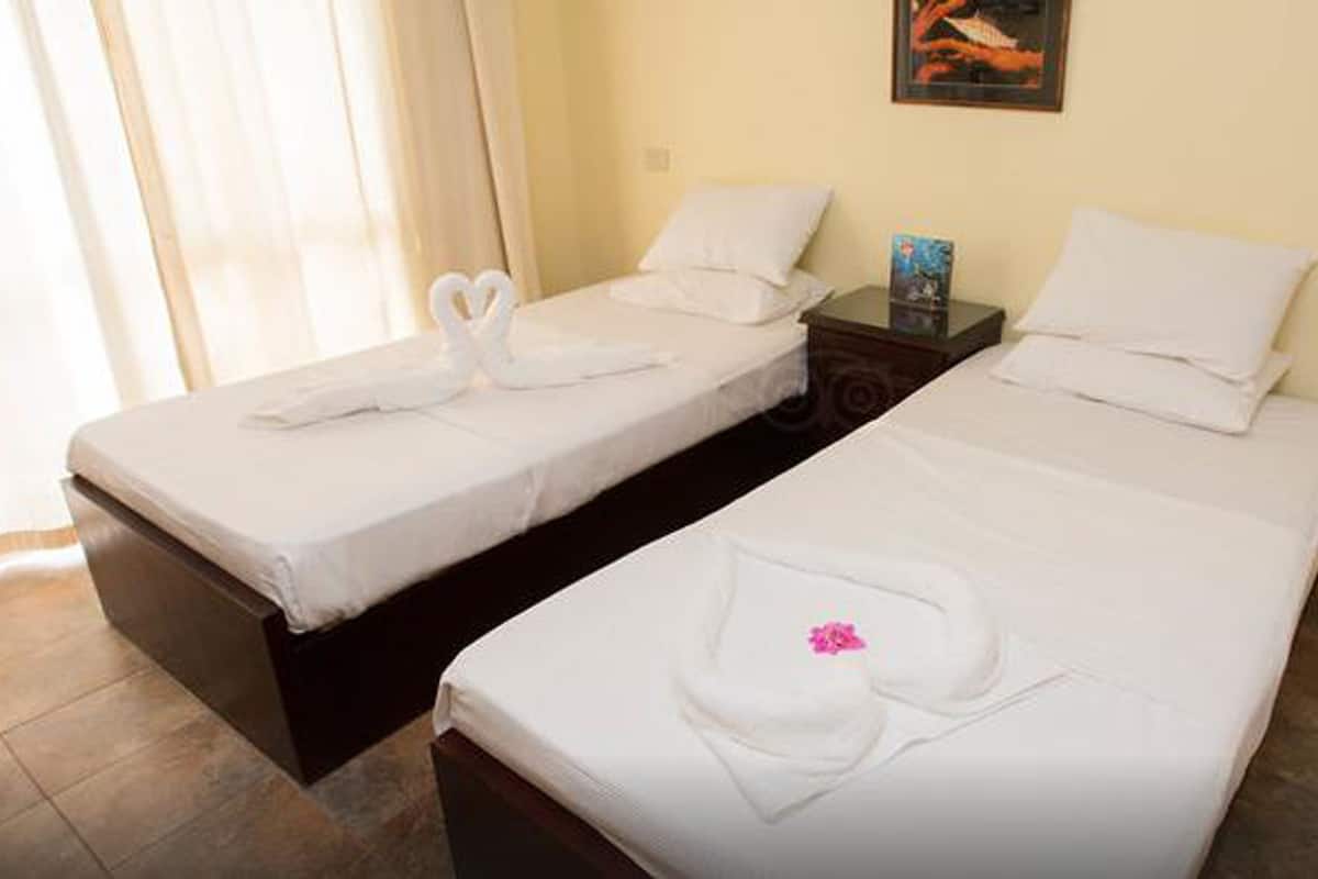 Two single beds with white linens and heart-shaped towels, a nightstand with a book, and a painting on the wall.