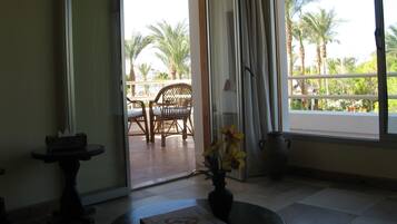 A room with a view of palm trees through a sliding glass door, a small table with a vase of flowers, and a chair.