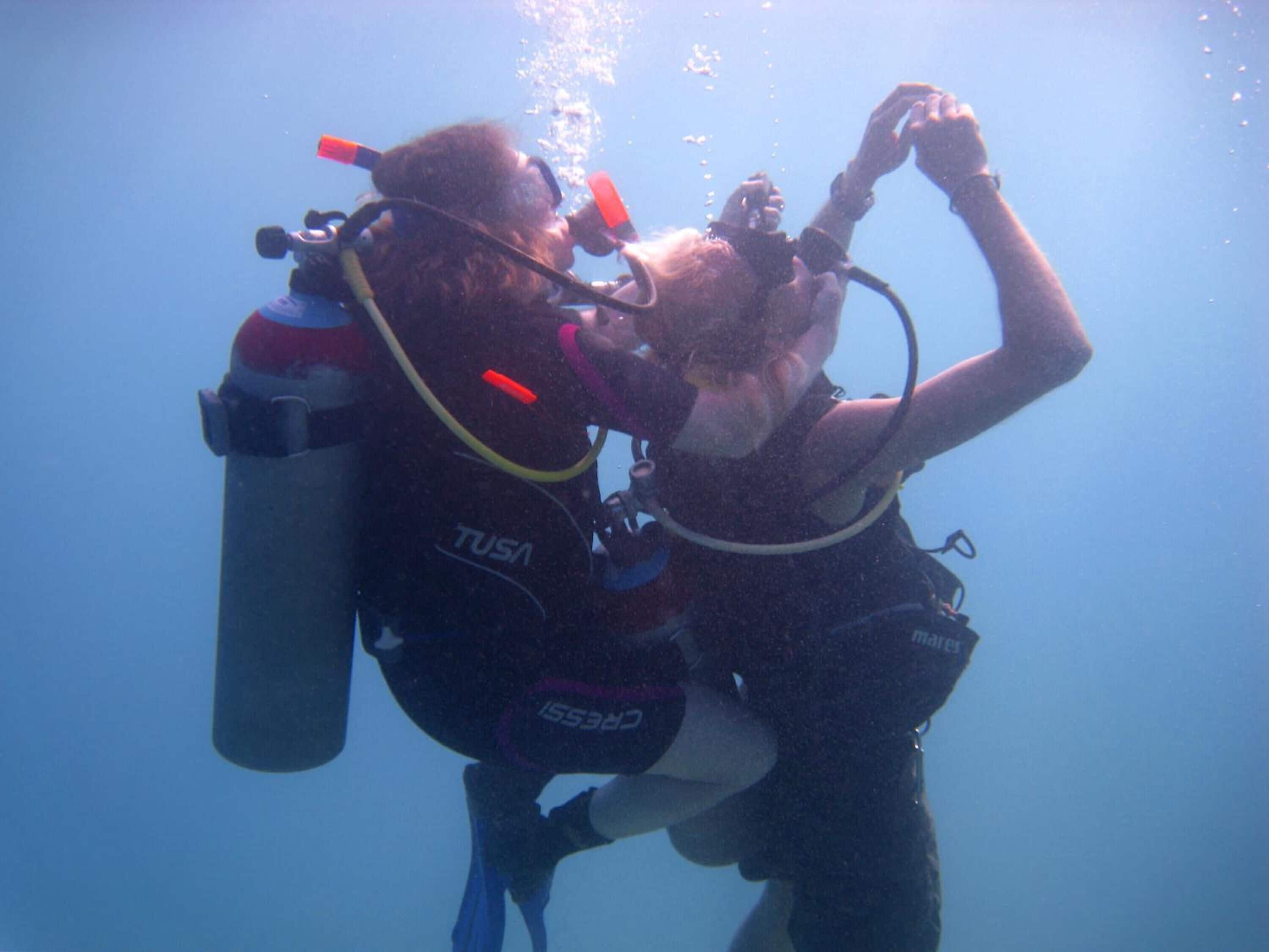 Dos personas bajo el agua, con equipo de buceo y tomadas de la mano.