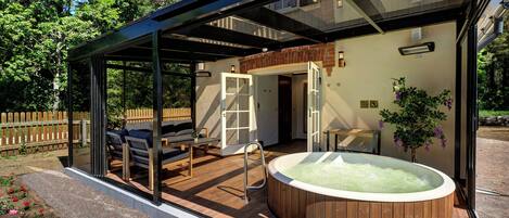 A glass-enclosed outdoor area with a hot tub, seating, and a wooden deck.