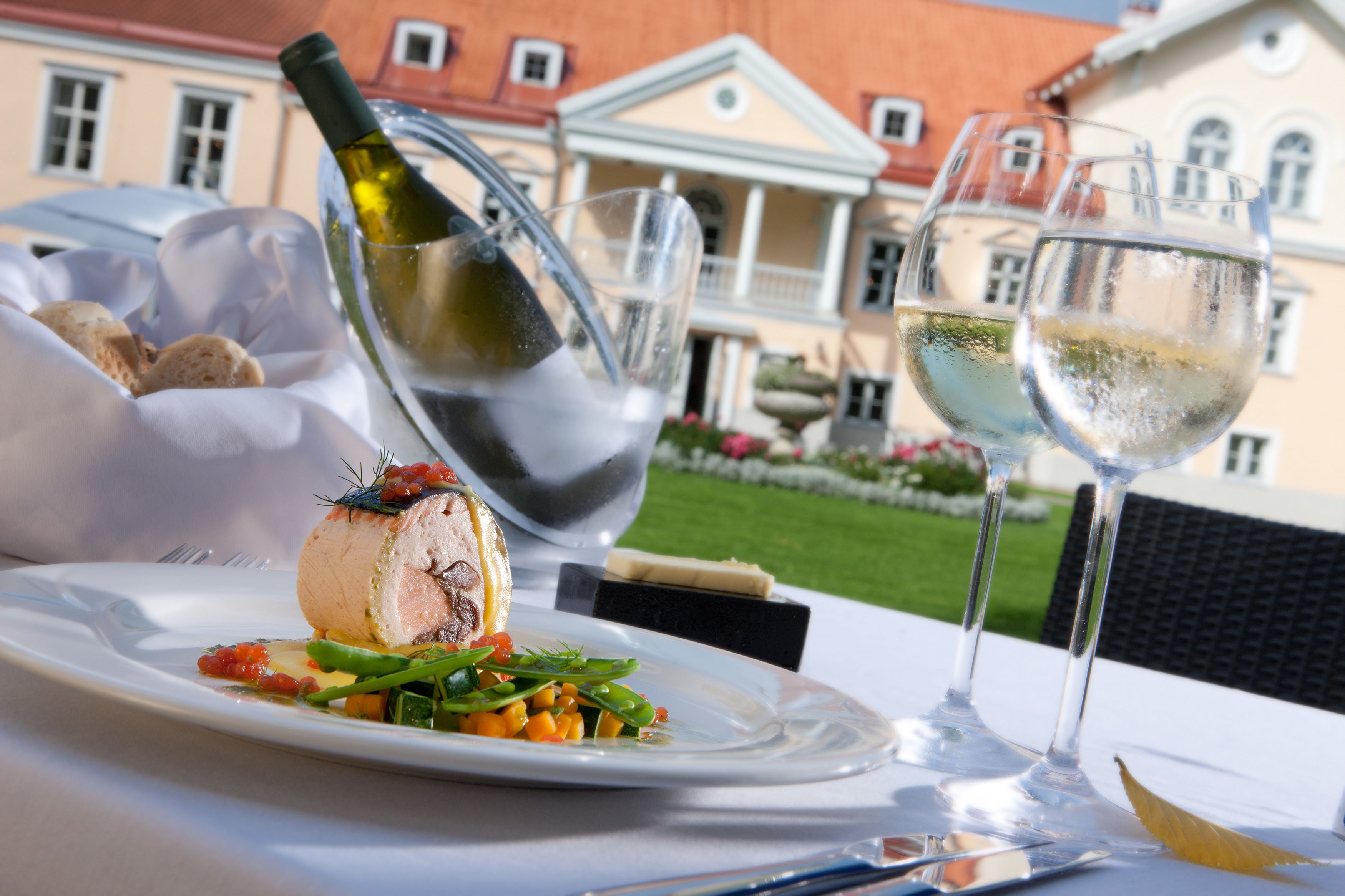 A dining table with a plate of food, a bottle of wine, and two glasses of wine.