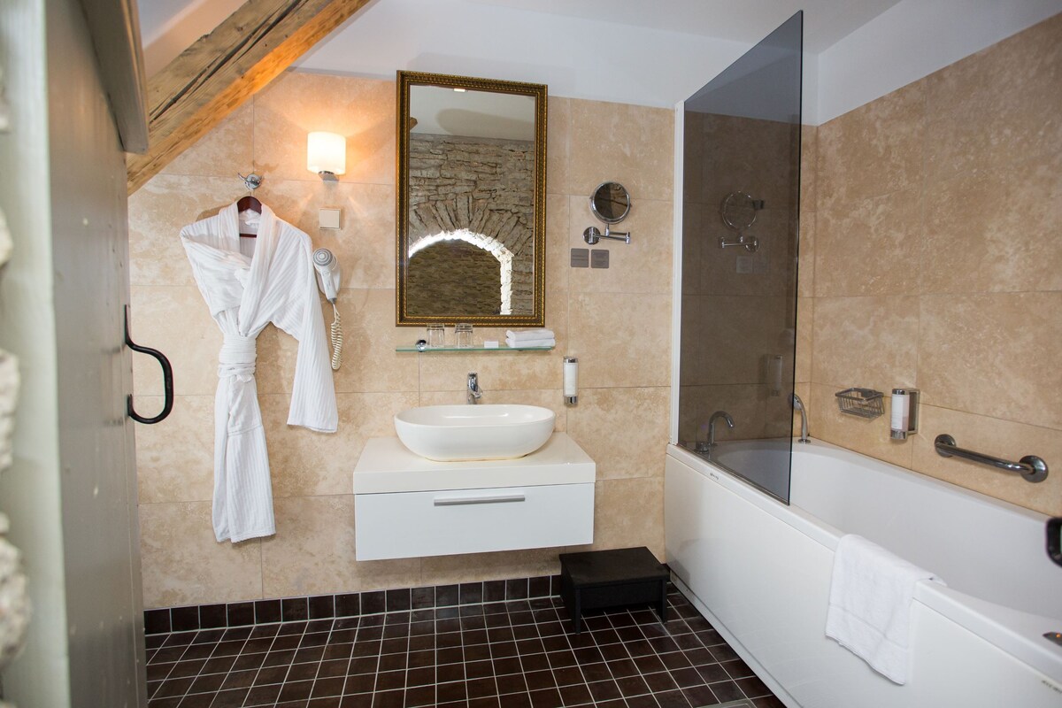 A modern bathroom with a large mirror, a white sink, a glass-enclosed shower, and a black tiled floor.