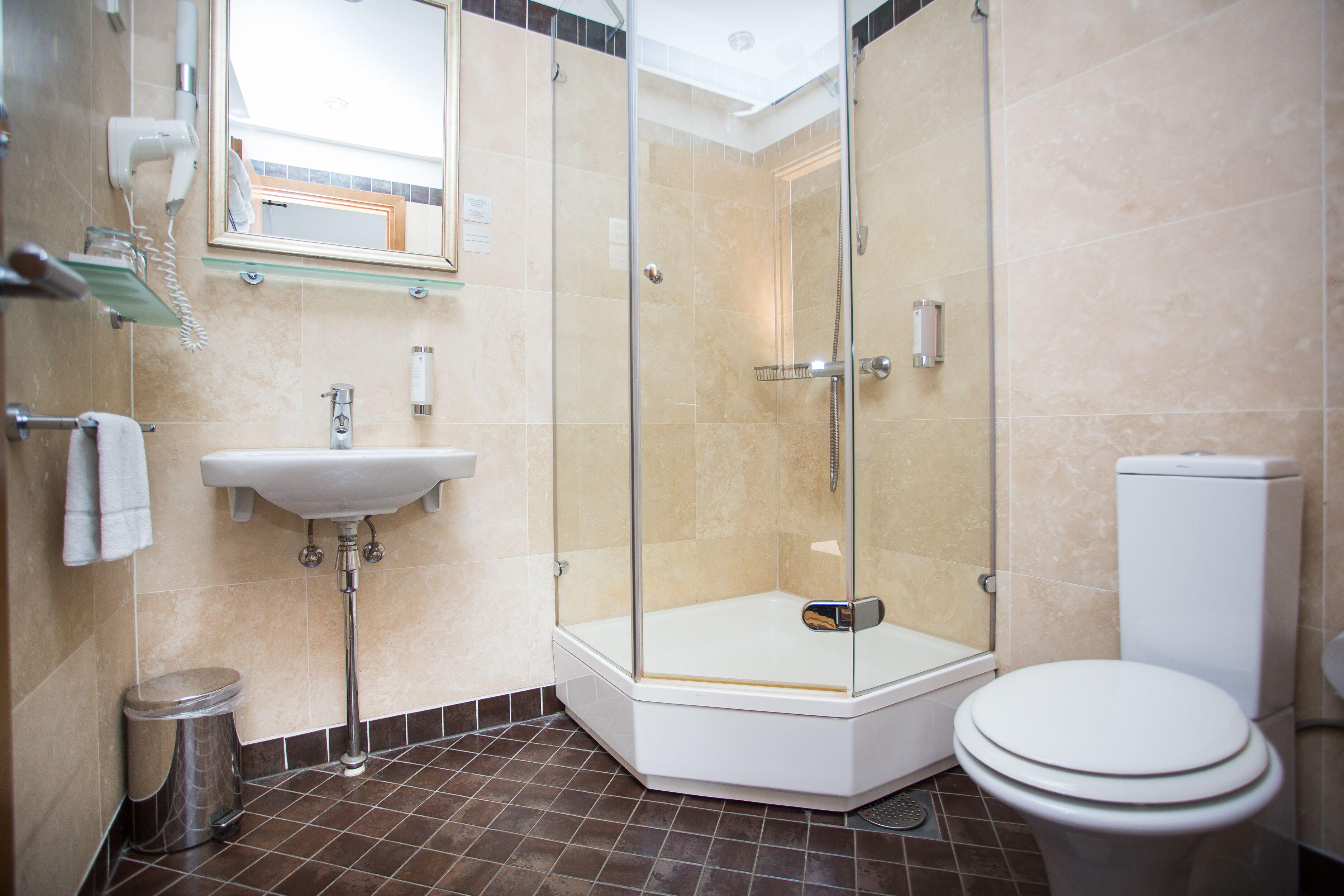 Un baño moderno con ducha envuelta en vidrio, lavamanos pedestal y retrete.