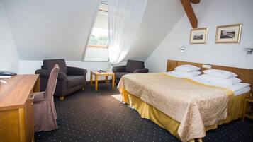 Une chambre d’hôtel avec un lit, deux fauteuils, un bureau et une fenêtre avec des rideaux.