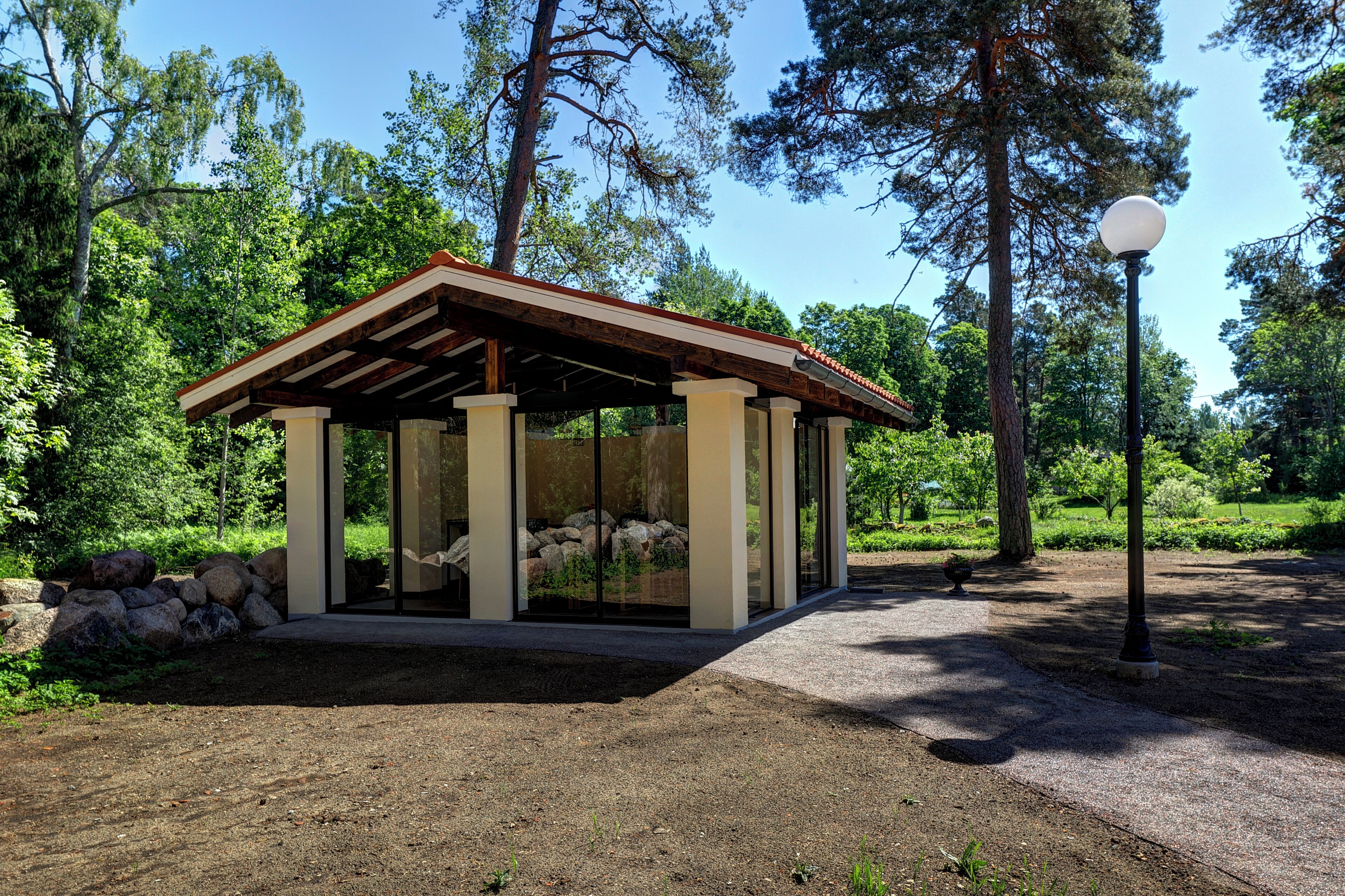 Un padiglione vetrato con tetto in legno, immerso in un paesaggio naturale tra alberi e rocce.