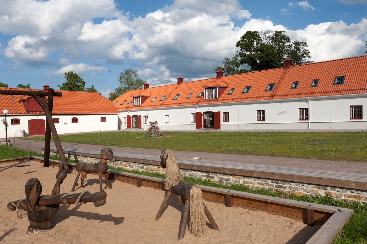 A traditional building with a red-tiled roof and white walls, featuring a stable with wooden horseshoes and a swing set.