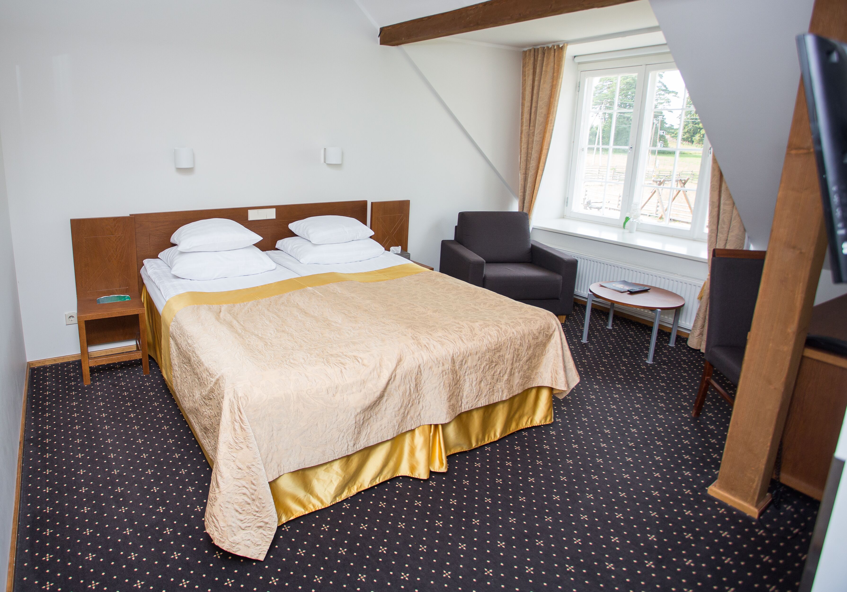 A hotel room with a bed, a chair, a small table, and a window.