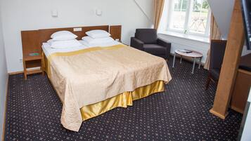 A hotel room with a bed, a chair, a small table, and a window.