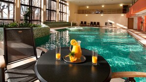 Une piscine intérieure à l’eau claire, entourée d’espaces aménagés pour s’asseoir et dotée de grandes fenêtres.