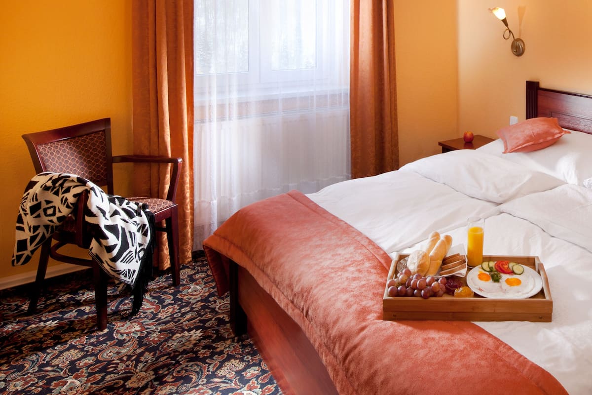 Une chambre d’hôtel avec un grand lit, une table de chevet en bois, une chaise recouverte d’un plaid à motifs et un plateau contenant des articles pour le petit-déjeuner.
