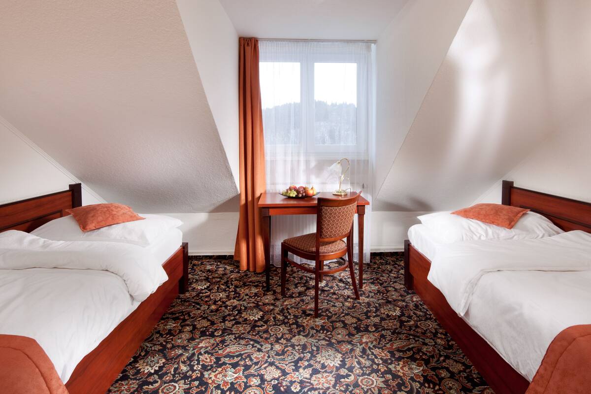 Une chambre d’hôtel avec deux lits, une petite table et une chaise, ainsi qu’une fenêtre avec des rideaux.
