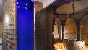 Une salle de bain moderne avec des murs recouverts de mosaïques, un lavabo central et une zone de douche éclairée en bleu.