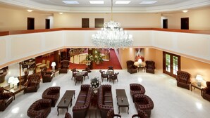 Un hall d’entrée spacieux, agrémenté d’un lustre, de canapés en cuir et d’un tapis rouge menant à un escalier.