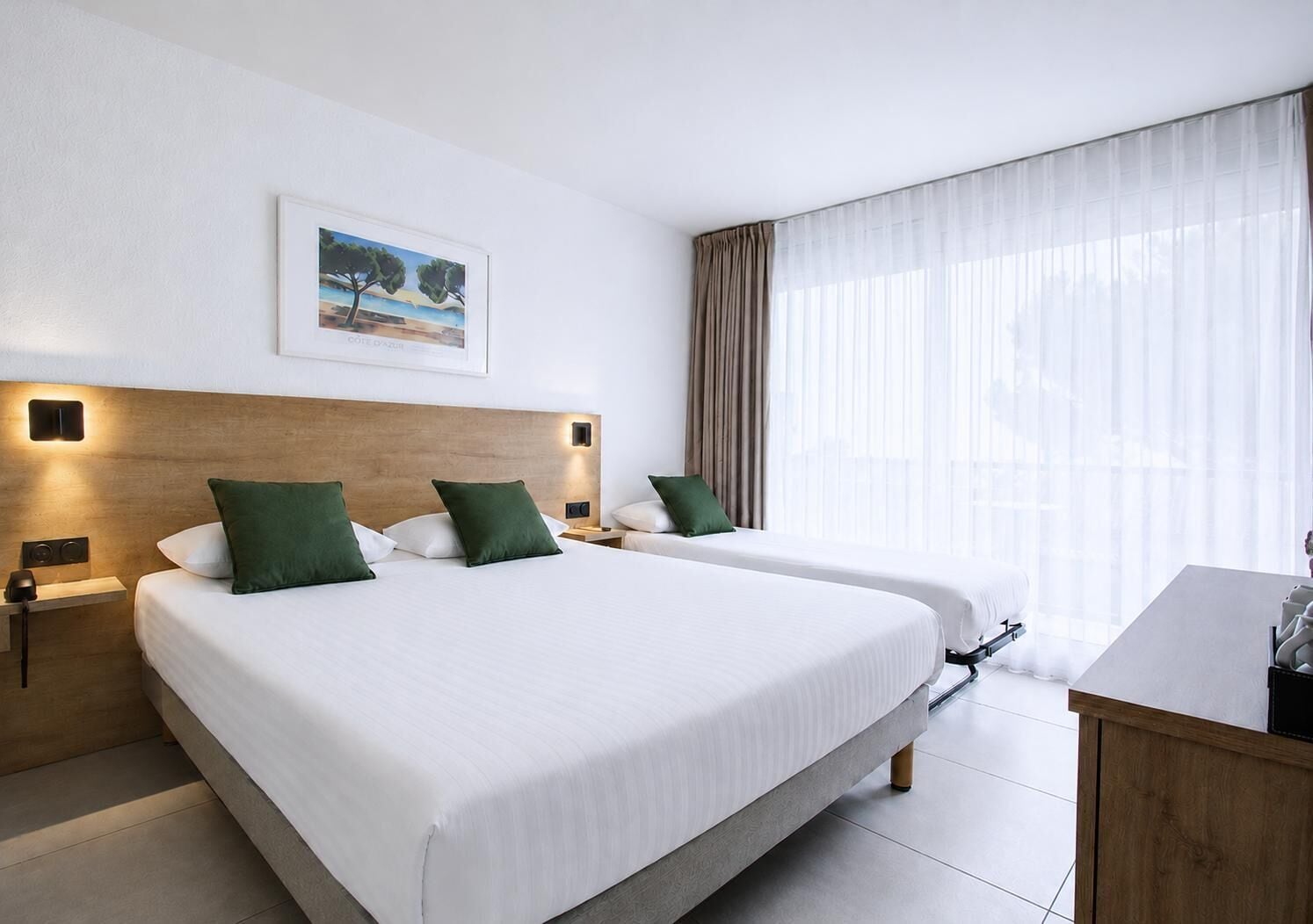 Habitación de hotel con dos camas, cabecero de madera, un cuadro y un amplio ventanal con cortinas.