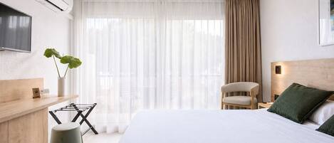 Una habitación de hotel con una cama, una silla, un escritorio con una planta y un televisor montado en la pared.