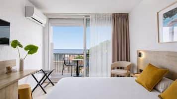 A hotel room with a bed, a desk, a chair, a plant, and a balcony with a view.