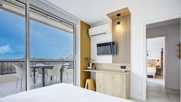 Una habitación de hotel moderna con una cama grande, un escritorio con una silla, un televisor montado en la pared y un balcón con mesa y sillas.