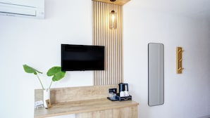 Una habitación de hotel moderna con una mesa consola de madera, un televisor de pantalla plana, un espejo, una lámpara de pared y una planta en maceta.