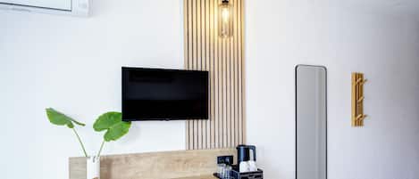 A modern hotel room with a wooden console table, a flat-screen TV, a mirror, a wall-mounted light fixture, and a potted plant.