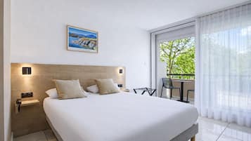 Habitación de hotel con una cama grande, una mesita con sillas, un balcón con vistas y un cuadro en la pared.