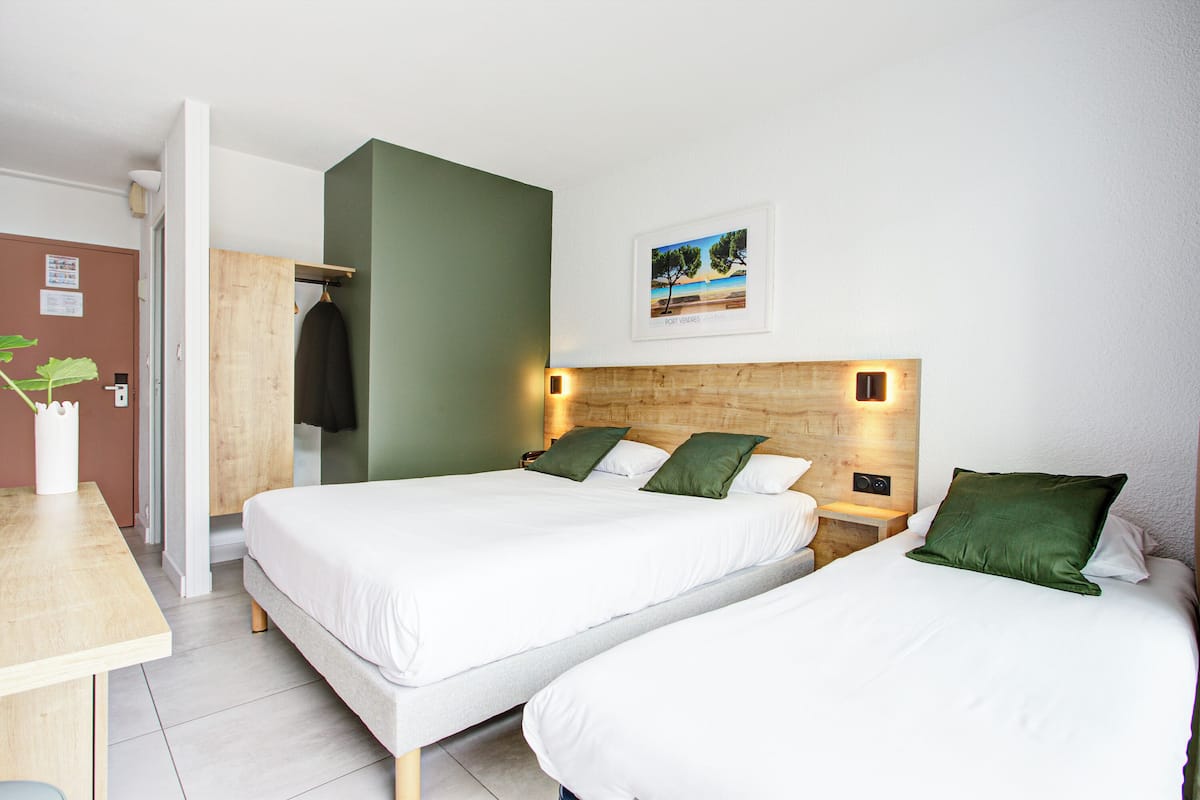 A hotel room with two beds, a wooden headboard, a small table, and a wall-mounted picture.