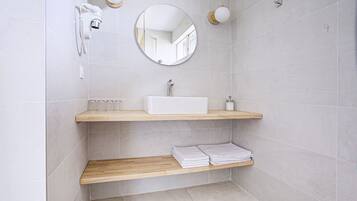 A modern bathroom with a white sink, wooden shelves, a round mirror, and a handheld showerhead.