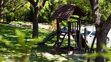 Children can play on the slide and climb the ladder in this park setting surrounded by trees and grass.