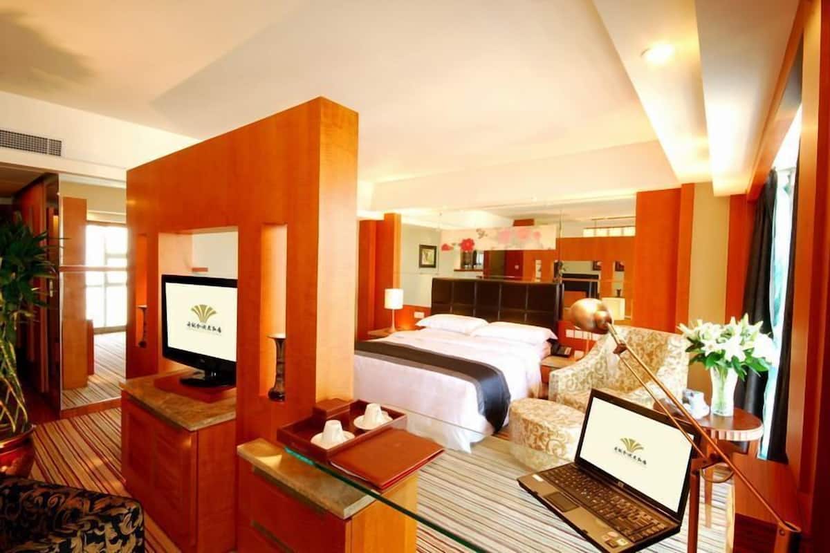 A hotel room with a bed, a desk with a laptop, a television, and a seating area with a chair and a table.